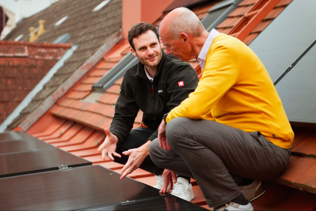 PV-Beratung: SolarNow-Berater im Gespräch mit einem Kunden auf einem Ziegeldach neben installierten Solarmodulen.