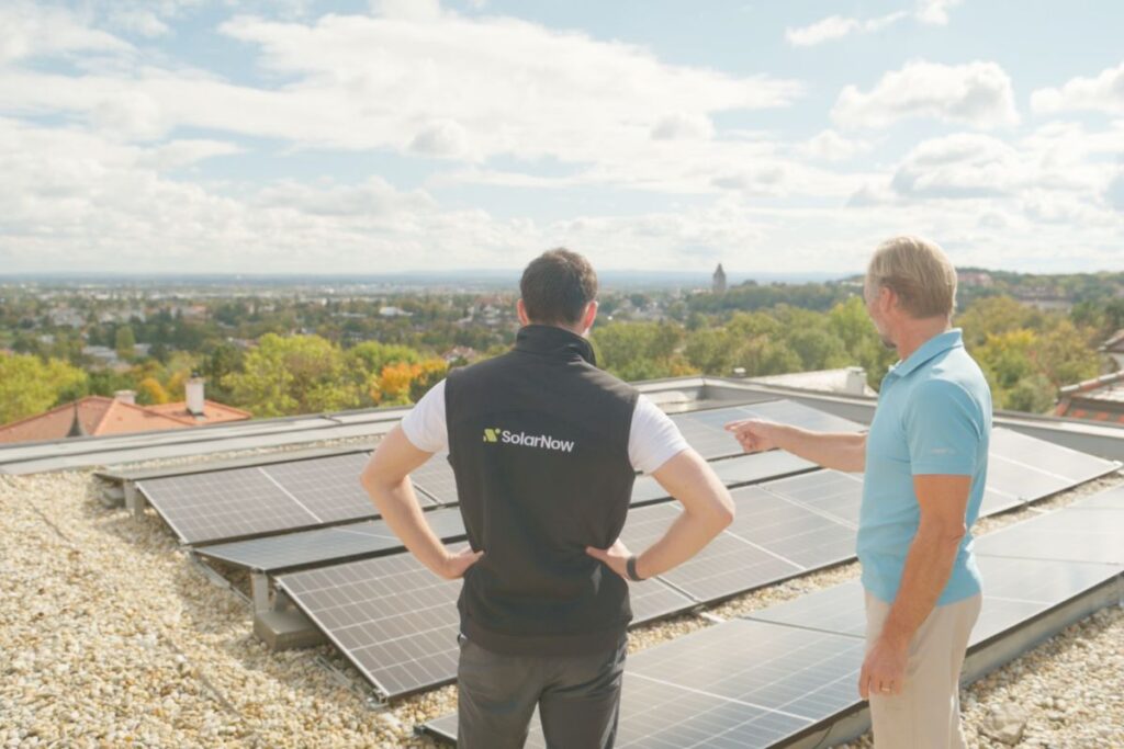 SolarNow-Berater im Gespräch mit einem Kunden auf einem Flachdach neben installierten Solarmodulen.