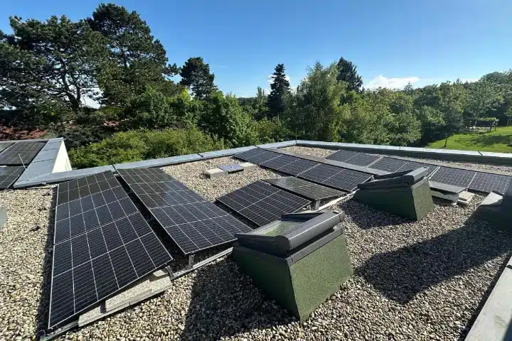 PV-Anlage Flachdach, Wien Umgebung Perchtoldsdorf. Solarmodule auf modernem Kiesdach mit Dachfenstern und Bäumen im Hintergrund.