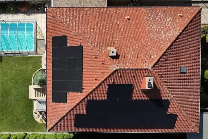 PV-Anlage auf Flachdach in Wien Umgebung Schwadorf. Solarpaneele auf rotem Ziegeldach mit Pool im Garten. Vogelperspektive.