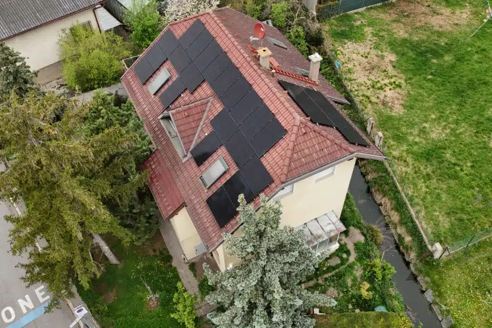 PV Anlage Vösendorf effiziente Solarlösung von SolarNow auf einem Einfamilienhaus mit rötlichem Ziegeldach, einer roten Satellitenschüssel und einem kleinen Bachlauf am Grundstücksrand, installiert von SolarNow