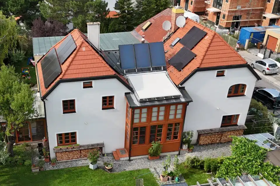 PV Anlage auf Schrägdach in Mödling SolarNow auf einem weißen Einfamilienhaus mit rotem Ziegeldach, Solarthermie-Kollektoren und einem markanten Wintergarten aus Holz, installiert von SolarNow