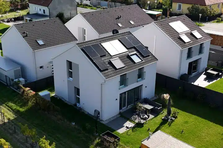PV-Anlage auf modernem Einfamilienhaus in Oyenhausen zeigt eine Luftaufnahme von drei identischen weißen Neubauhäusern mit grauen Satteldächern, wobei das mittlere Haus mit Full-Black Solarmodulen bestückt ist, installiert von SolarNow