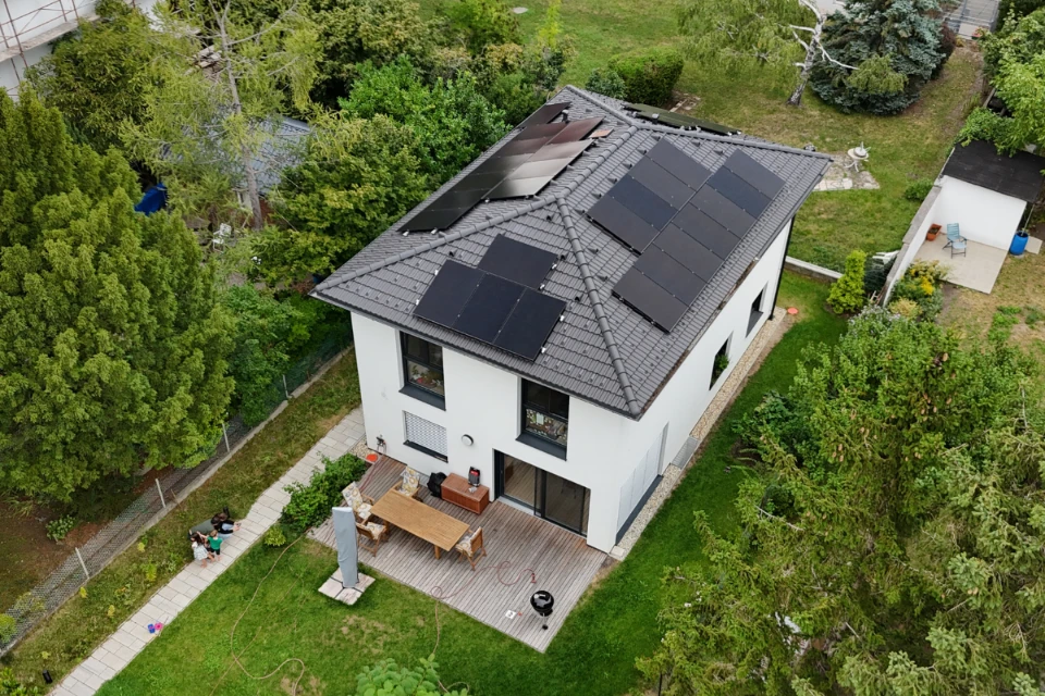 Photovoltaikanlage auf Einfamilienhaus in Wien Liesing auf einem zweistöckigen Neubau mit grauem Walmdach, Holzterrasse und spielenden Kindern im Garten, installiert von SolarNow