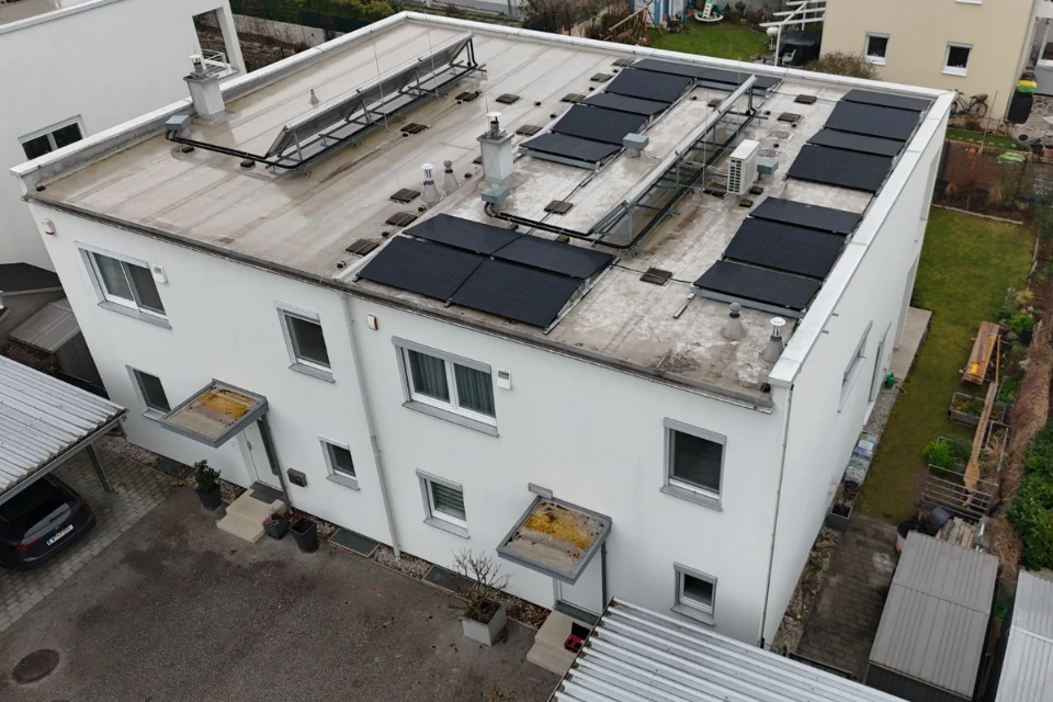 Referenz SolarNow PV Anlage auf Flachdach in Perchtoldsdorf auf einem zweistöckigen weißen Wohngebäude mit Flachdach, kleinen Vordächern über den Eingängen und installierten Klimageräten, installiert von SolarNow