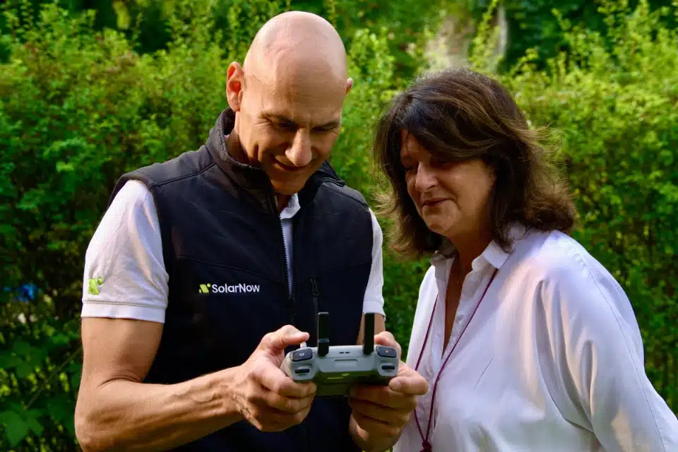 SolarNow Mitarbeiter demonstriert einer Kundin den Drohneneinsatz zur präzisen Photovoltaikplanung in Wien und Umgebung.