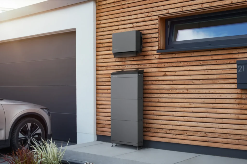Stromspeicher und Wechselrichter der Marke EcoFlow Power Ocean an der Fassade eines Hauses neben einem geparkten Elektroauto.